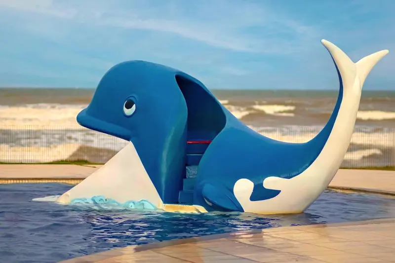 Escorregador em forma de baleia na piscina infantil, com o mar ao fundo