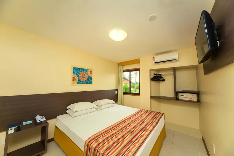 Quarto do bangalô com cama de casal, TV, ar-condicionado e colcha listrada