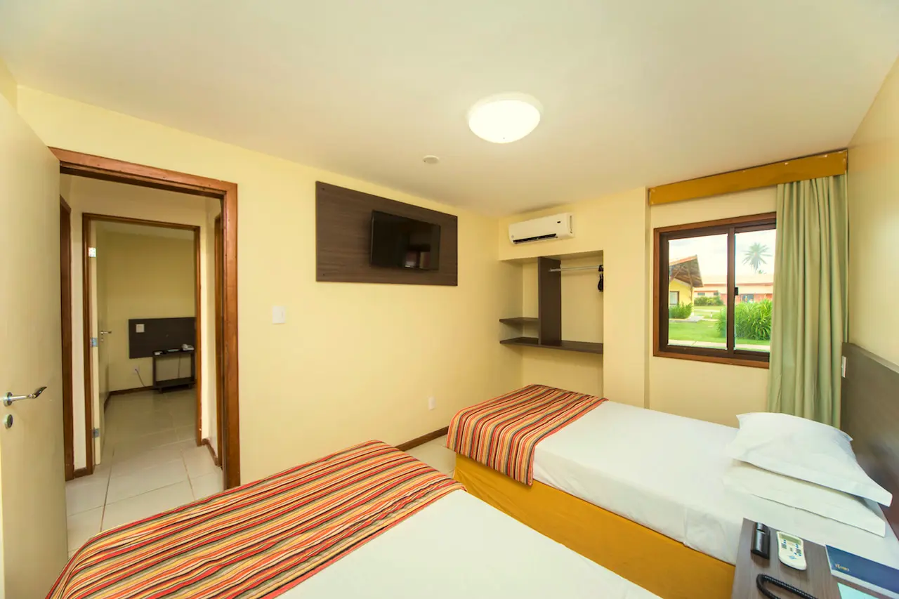 Quarto do bangalô com cama de solteiro, TV e porta aberta para o outro quarto