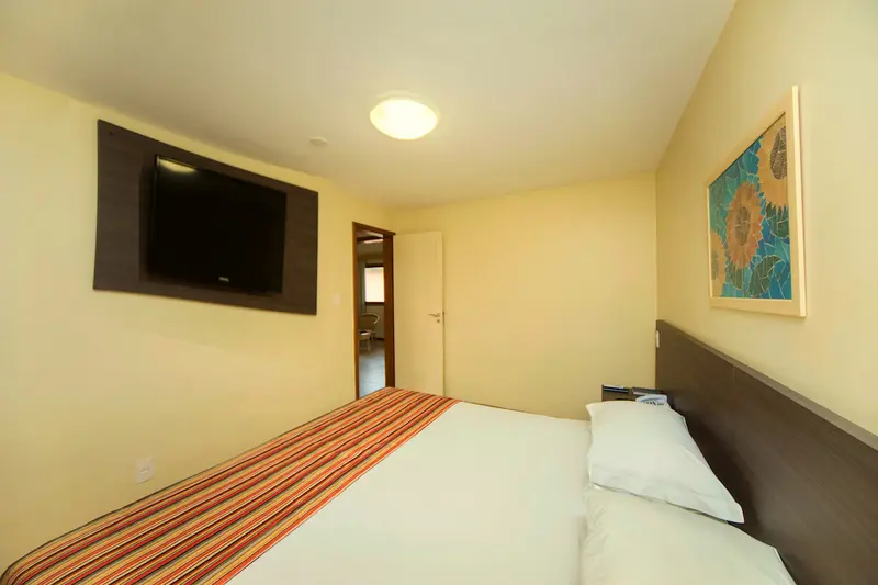 Quarto do bangalô com cama de casal, TV na parede e quadro de flores