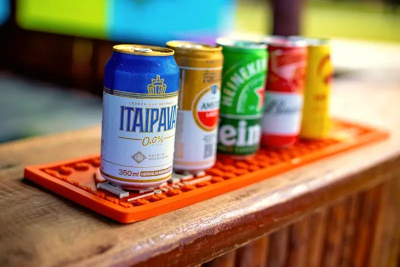 Cinco latas de cerveja alinhadas sobre um tapete de bar laranja no balcão de madeira