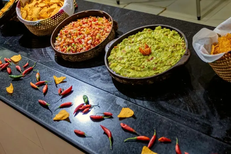 Tigelas de guacamole e molhos com nachos, cercadas por pimentas