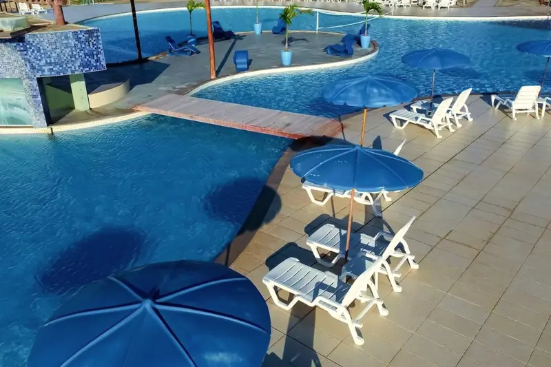 Piscina vista do alto com guarda-sóis azuis e espreguiçadeiras brancas