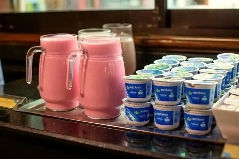 Jarras de vitamina rosa e potinhos de iogurte na bancada do bufê