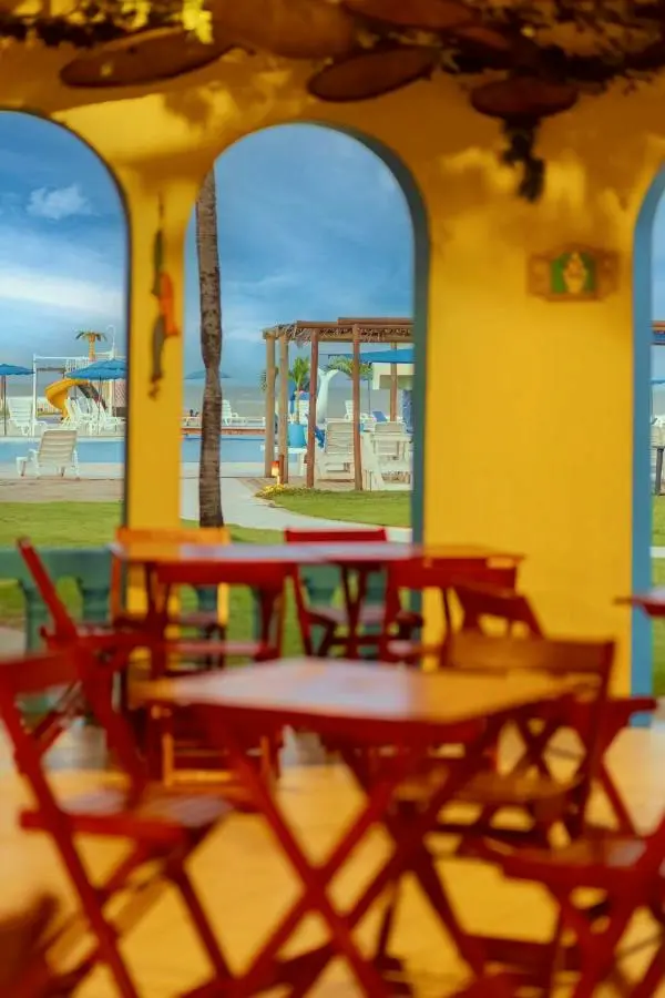 Pátio com mesas e cadeiras vermelhas, janelas em arco e vista para a área da piscina