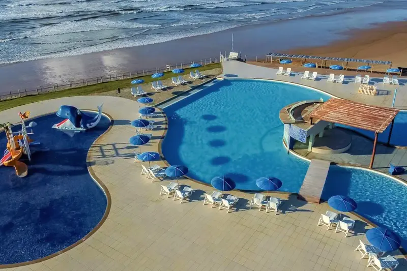 Vista aérea da piscina de curvas com guarda-sóis, a praia e o mar ao lado