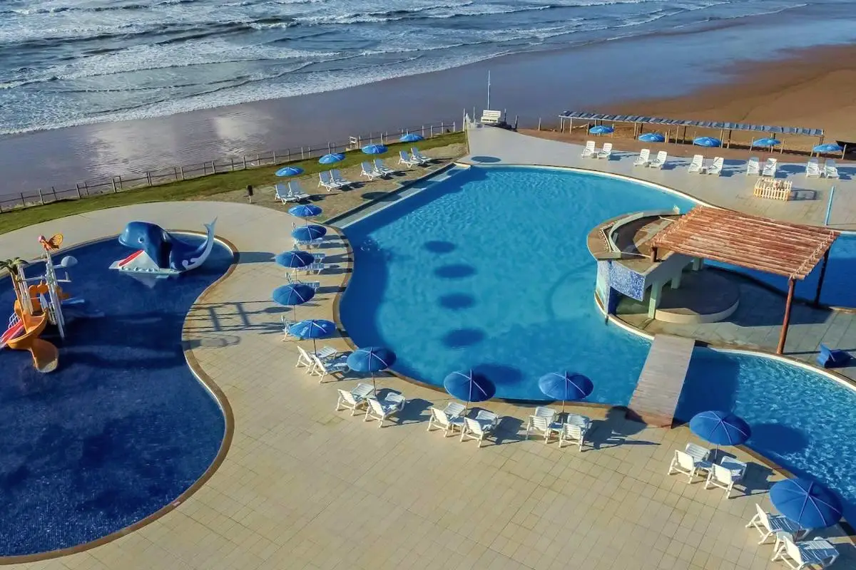 Vista aérea da piscina de curvas com guarda-sóis, a praia e o mar ao lado