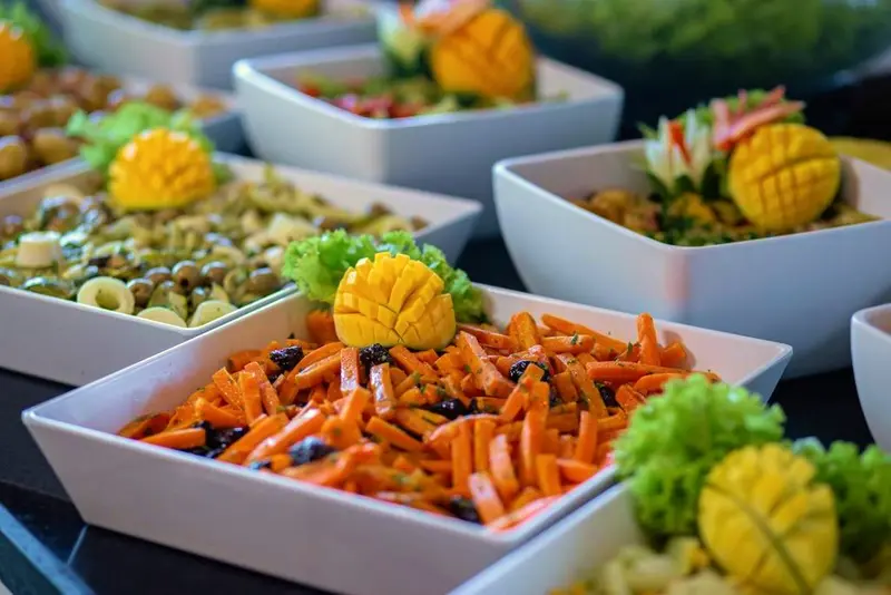 Tigelas brancas com saladas coloridas e frutas esculpidas