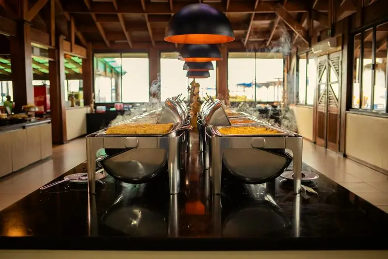 Restaurante com bufê em ilha central, cubas fumegantes e luminárias pretas