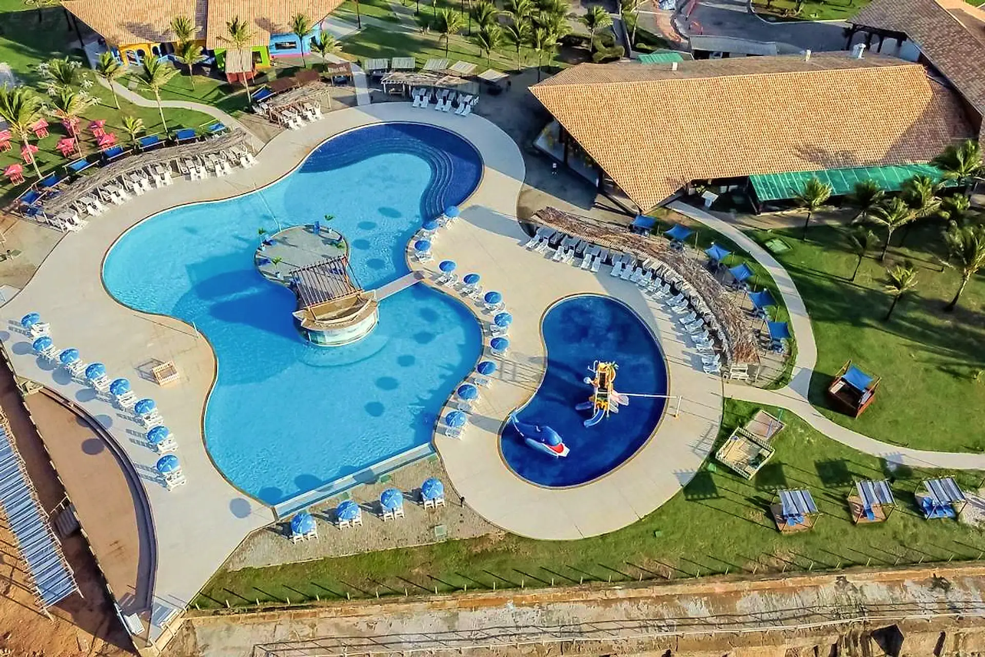 Vista aérea do complexo de piscinas cercado por gramado e coberturas de palha